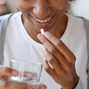 Black woman taking probiotic with glass of water